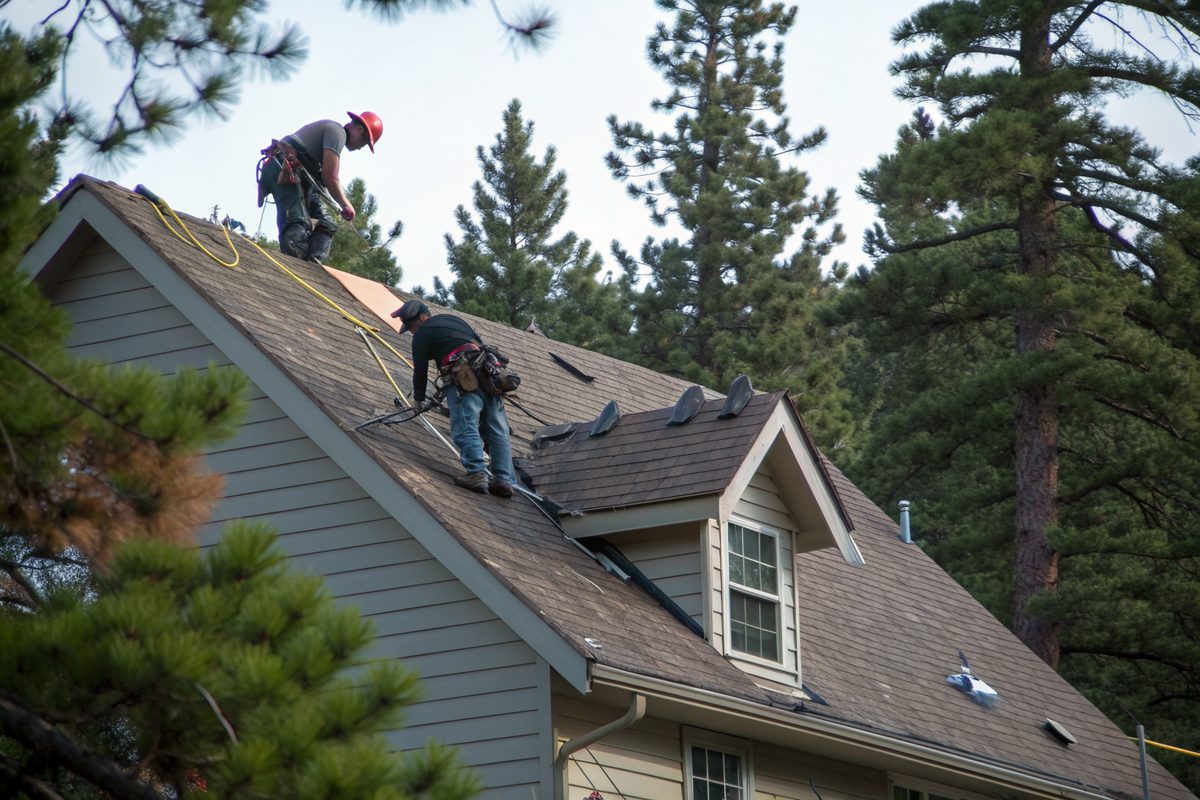 Two roofers laying new shingles on a two-story house